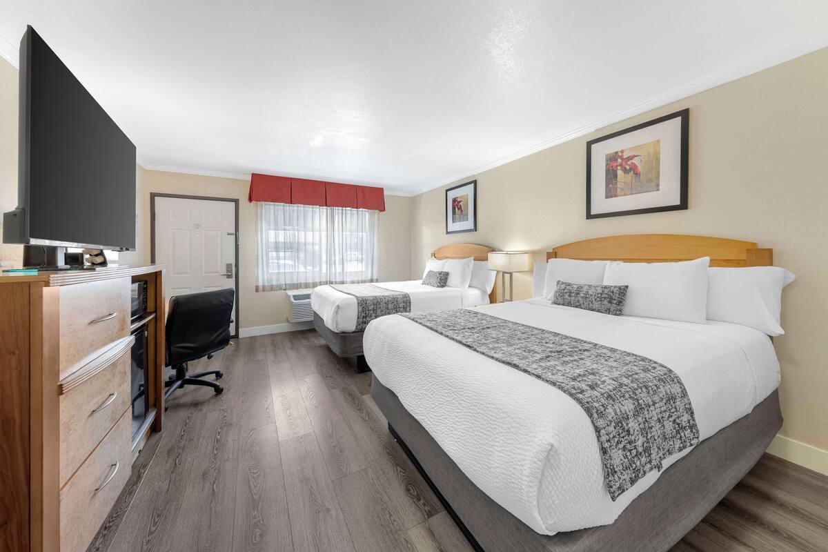 A hotel room with two beds, a desk with a computer, a TV, and a wardrobe.