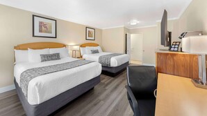 Une chambre d’hôtel avec deux lits, un bureau, une chaise et un téléviseur.