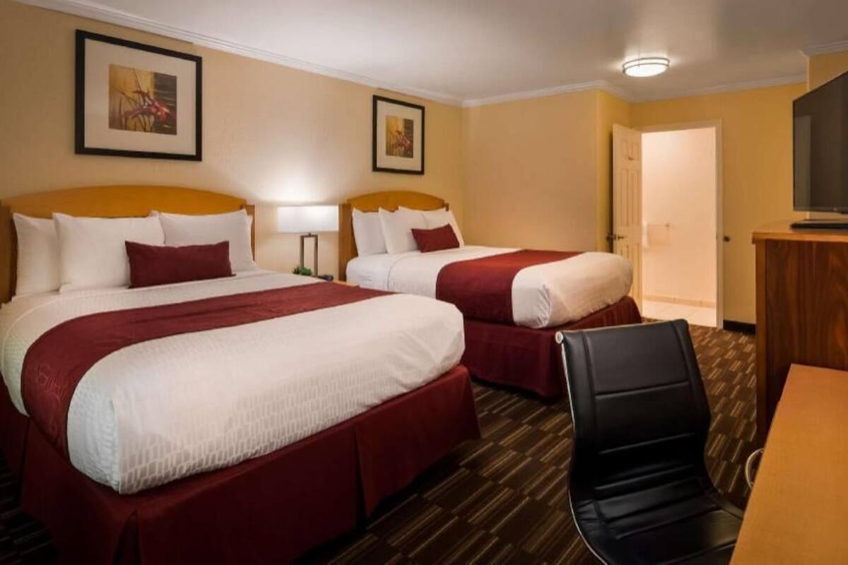 A hotel room with two beds, a desk, a chair, and a television.