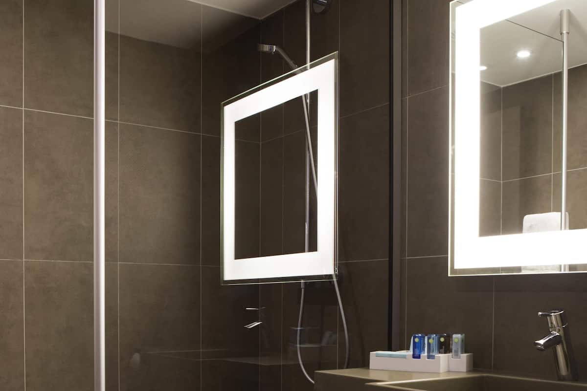 Et moderne badeværelse med et stort spejl, en brusekabine og en håndvask med toiletartikler.