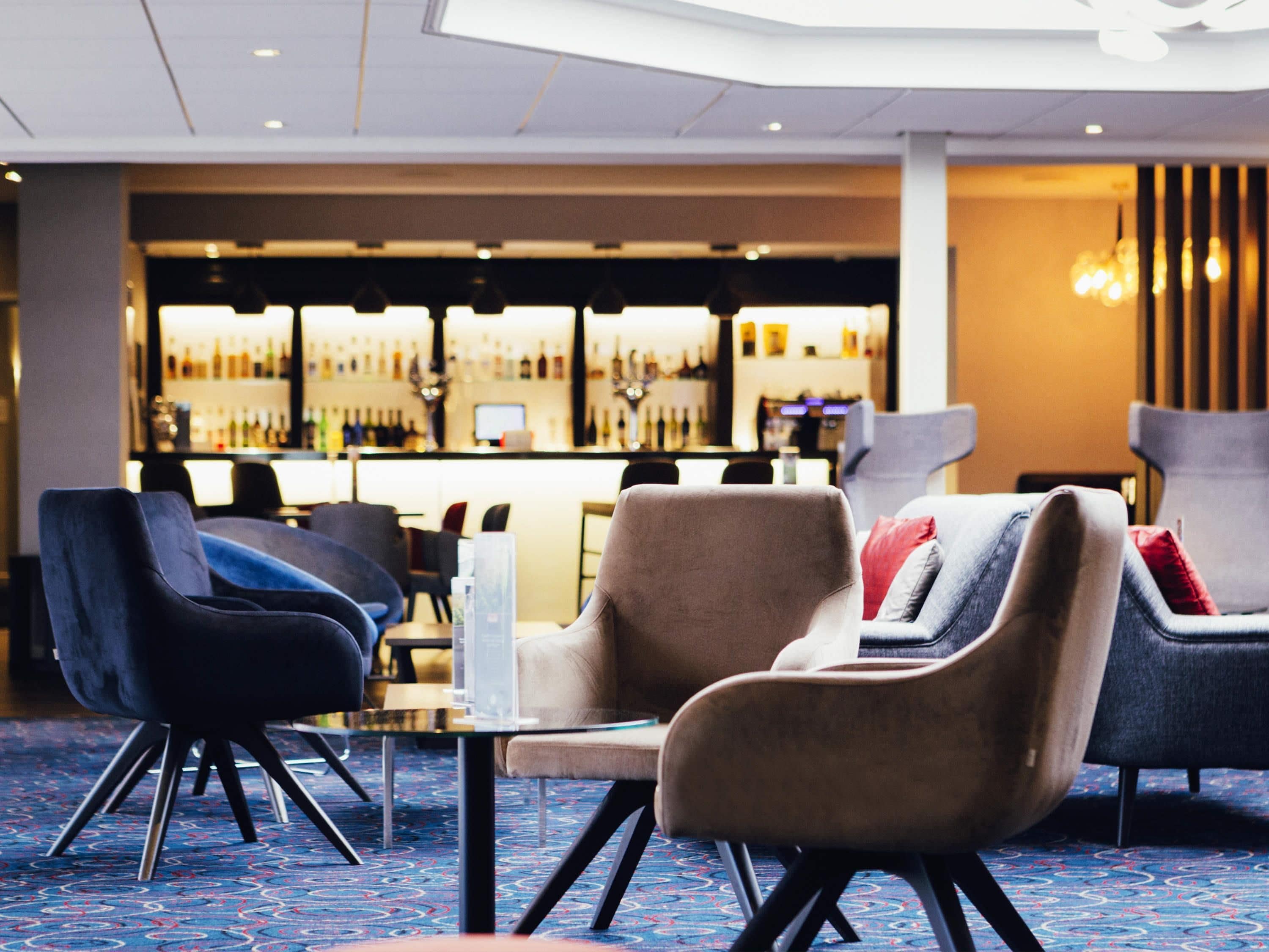 A modern hotel lobby with a bar area in the background.