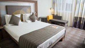 A hotel room with a large bed, a desk, a chair, and a nightstand.