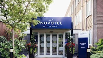 The Novotel hotel entrance with a glass door, a signboard, and potted plants.
