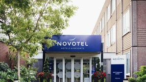 Novotel-hotellin sisäänkäynti, jossa on lasiovi, opastekyltti ja ruukkuistutettuja kasveja.