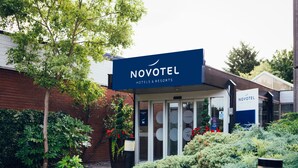 A Novotel hotel entrance with a glass door, surrounded by greenery and a brick wall.
