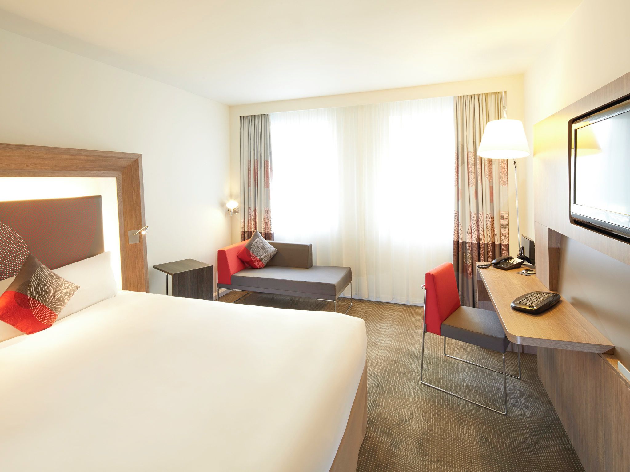 Een hotelkamer met een bed, een bureau met stoel, een tafeltje, een lamp en een televisie.