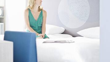 A woman sitting on a bed with a magazine, in a room with a modern design and a circular light fixture on the wall.