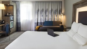 Hotellihuone, jossa on sänky, työpöytä kannettavalla tietokoneella, sohva, kahvinkeitin ja televisio.