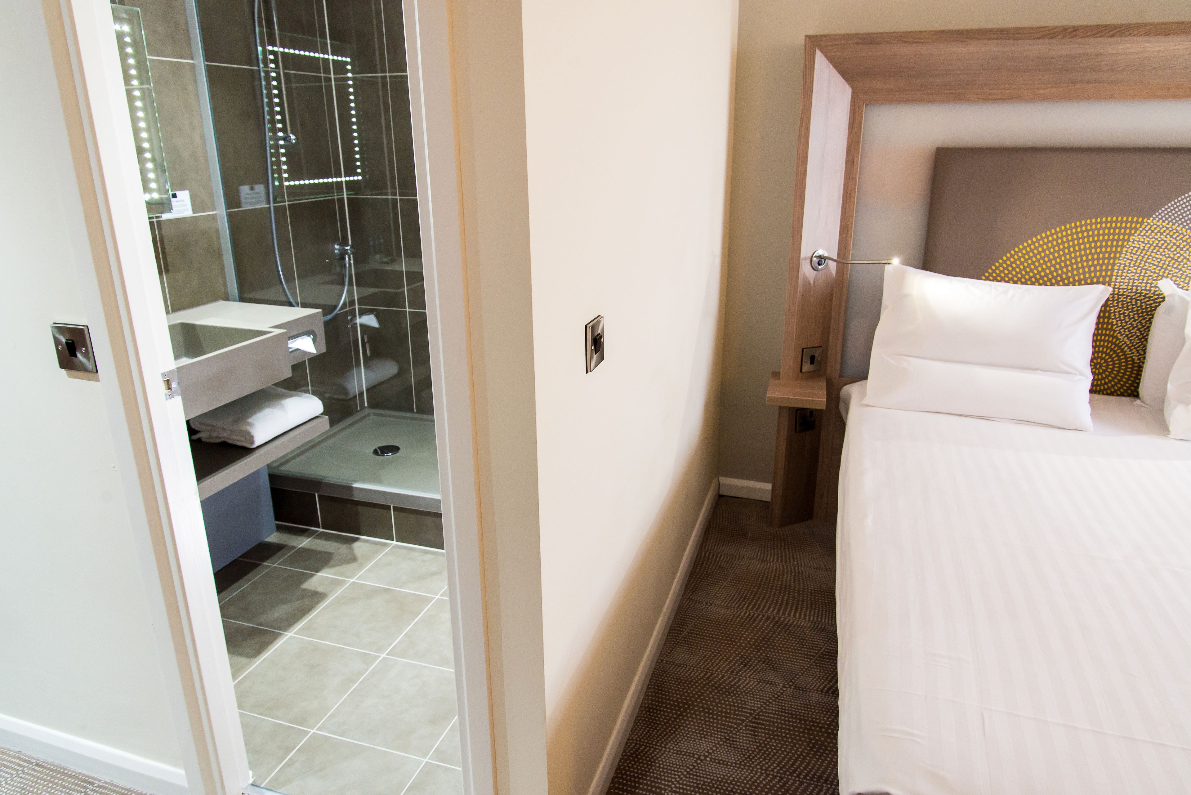 Et hotelværelse med bruser, toilet og en seng med sengegavl.