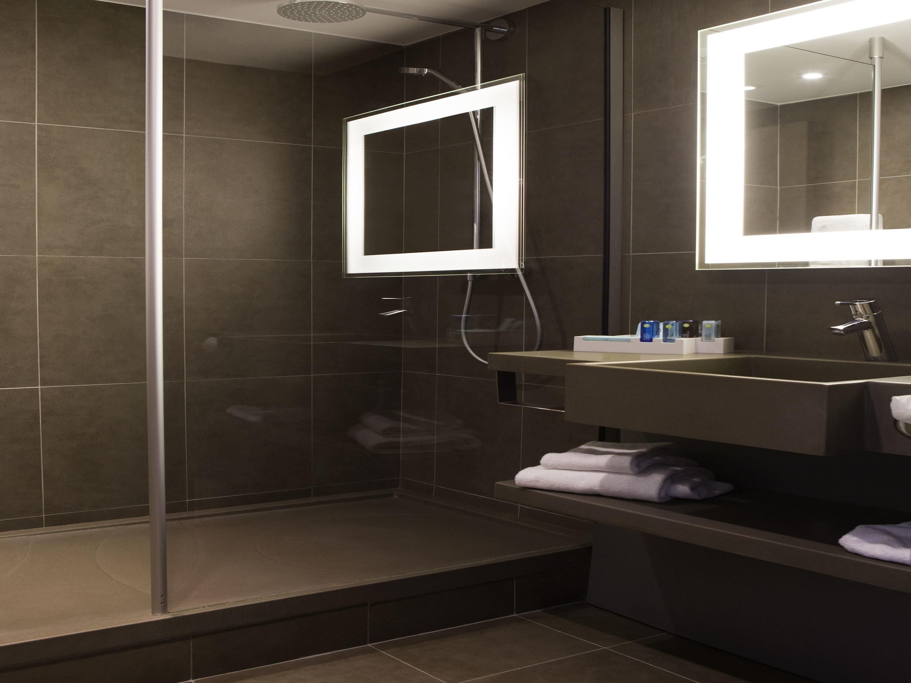 A modern bathroom with a glass-enclosed shower, a vanity with a mirror, and neatly folded towels.