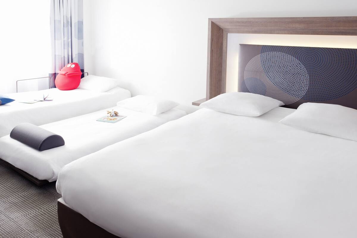 A hotel room with two beds, a red toy, a framed artwork, and a window with curtains.