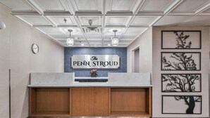 A reception area with a sign reading "The Penn Stroud," wooden cabinets, a clock, and framed tree artwork on the wall. - The Penn Stroud, Stroudsburg - Poconos, an Ascend Collection Hotel (Stroudsburg)