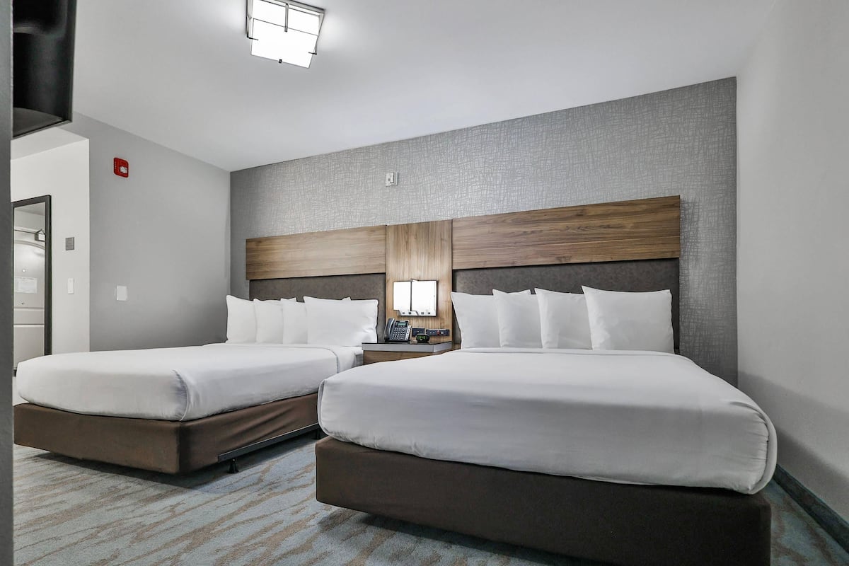 A hotel room with two beds, a wooden headboard, a bedside table with a phone, and a carpeted floor.