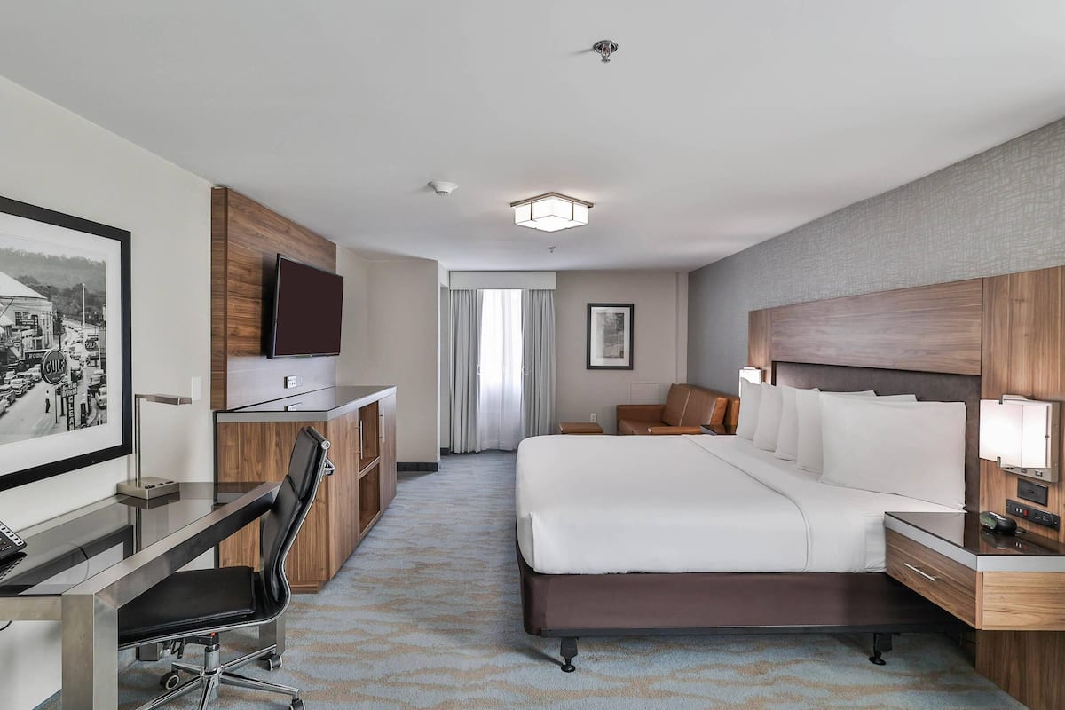 A hotel room with a bed, desk, chair, and a television.