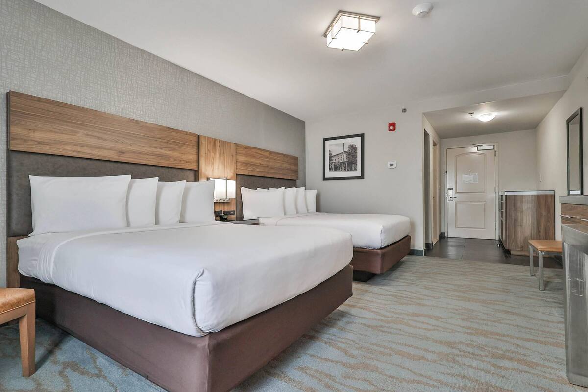 A hotel room with two beds, a desk, a chair, and a bathroom visible through an open door.