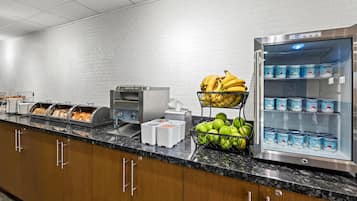 A breakfast bar with various food items, a refrigerator with yogurt, and a fruit basket.