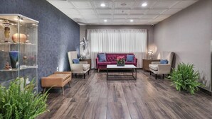A modern living room with a dark wood floor, a red sofa, two armchairs, a coffee table, and a glass display case with decorative items. - The Penn Stroud, Stroudsburg - Poconos, an Ascend Collection Hotel (Stroudsburg)