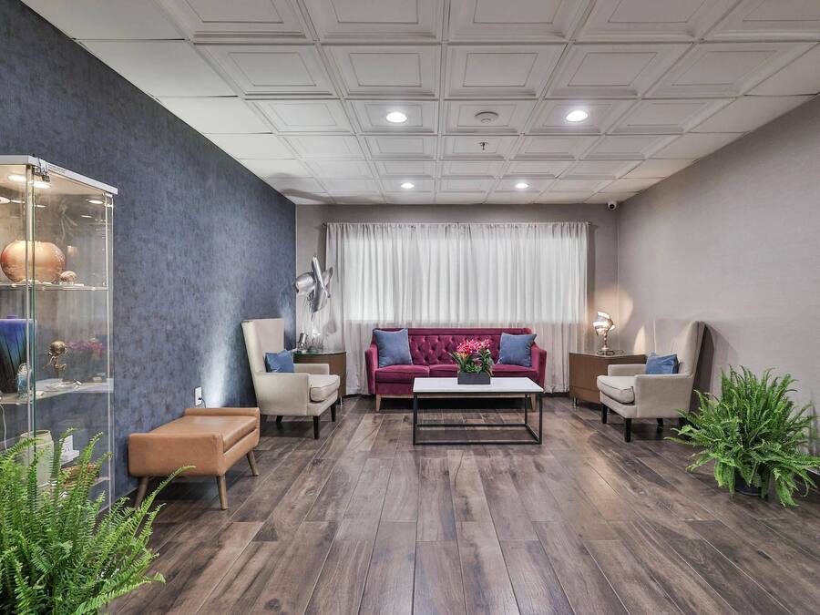 Ein modernes Wohnzimmer mit dunklem Holzboden, einem roten Sofa, zwei Sesseln, einem Couchtisch und einer Glasvitrine mit Dekoration.