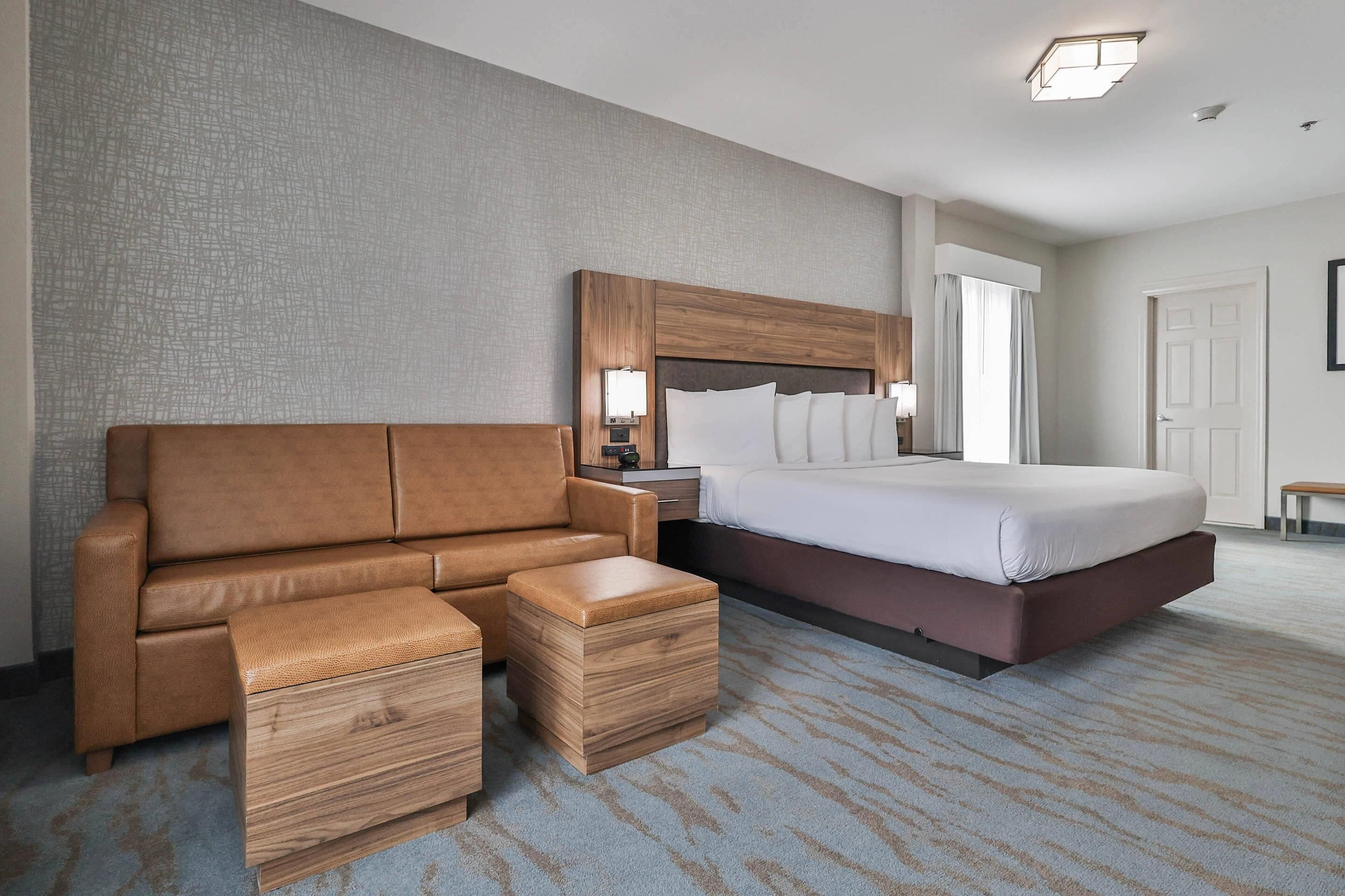 A hotel room with a large bed, a sofa, a wooden nightstand, and a small table.