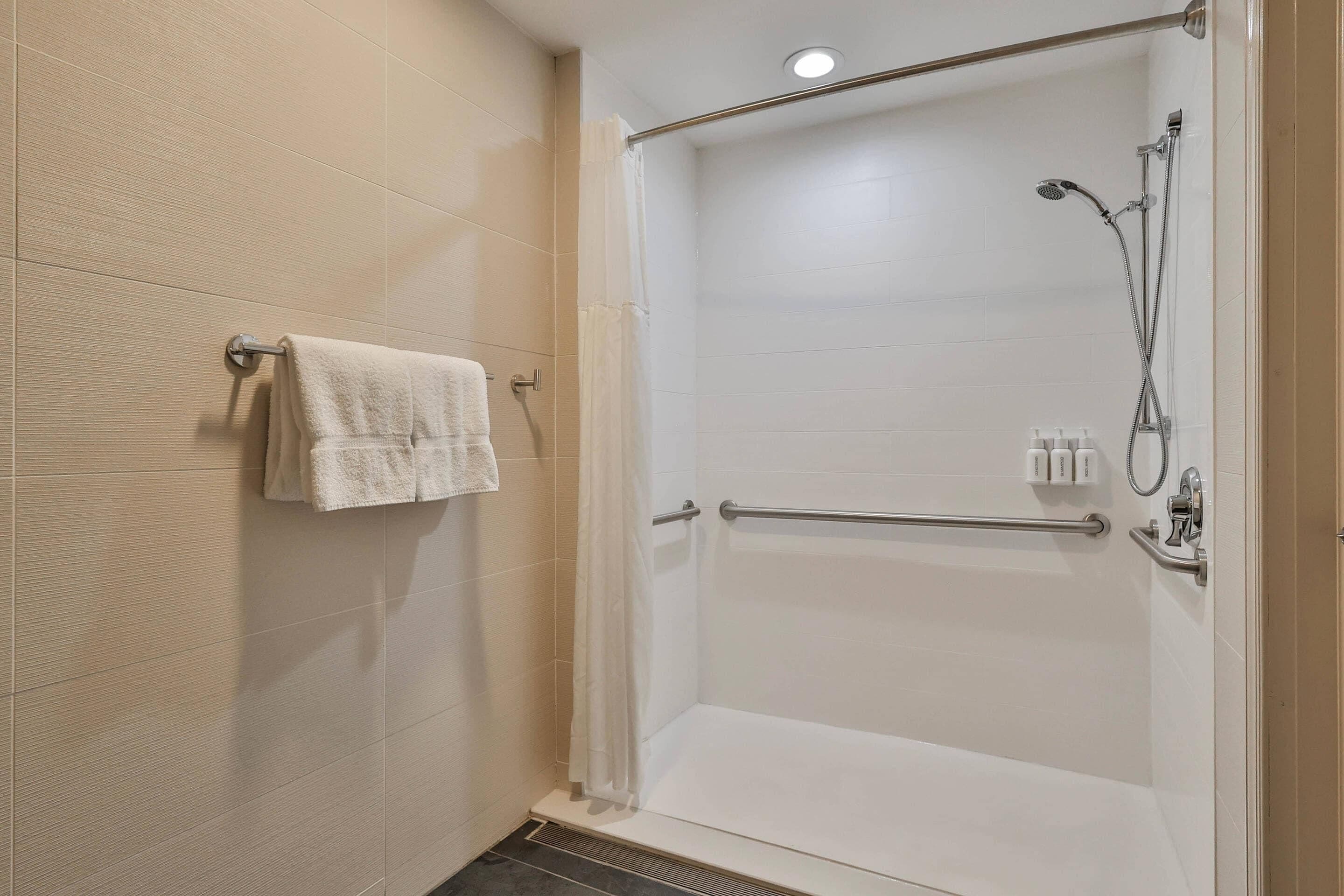 A modern shower area with a glass door, a towel rack, and a handrail.