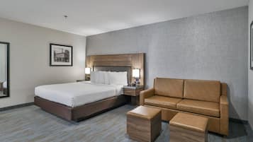 Quarto de hotel com uma cama grande, cabeceira de madeira, sofá de couro marrom, mesa de cabeceira de madeira e um quadro emoldurado na parede.