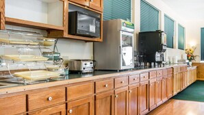 A kitchen with wooden cabinets, a microwave, a toaster, and a refrigerator. - Quality Inn & Suites Mackinaw City Beachfront (Mackinaw City)