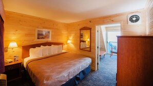 A wooden room with a bed, bedside lamps, a mirror, and a view of the outside balcony. - Quality Inn & Suites Mackinaw City Beachfront (Mackinaw City)
