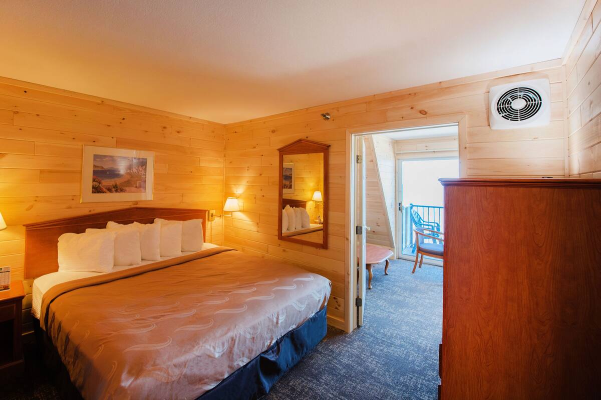 Una habitación de madera con una cama, lámparas de noche, un espejo y vistas al balcón exterior.