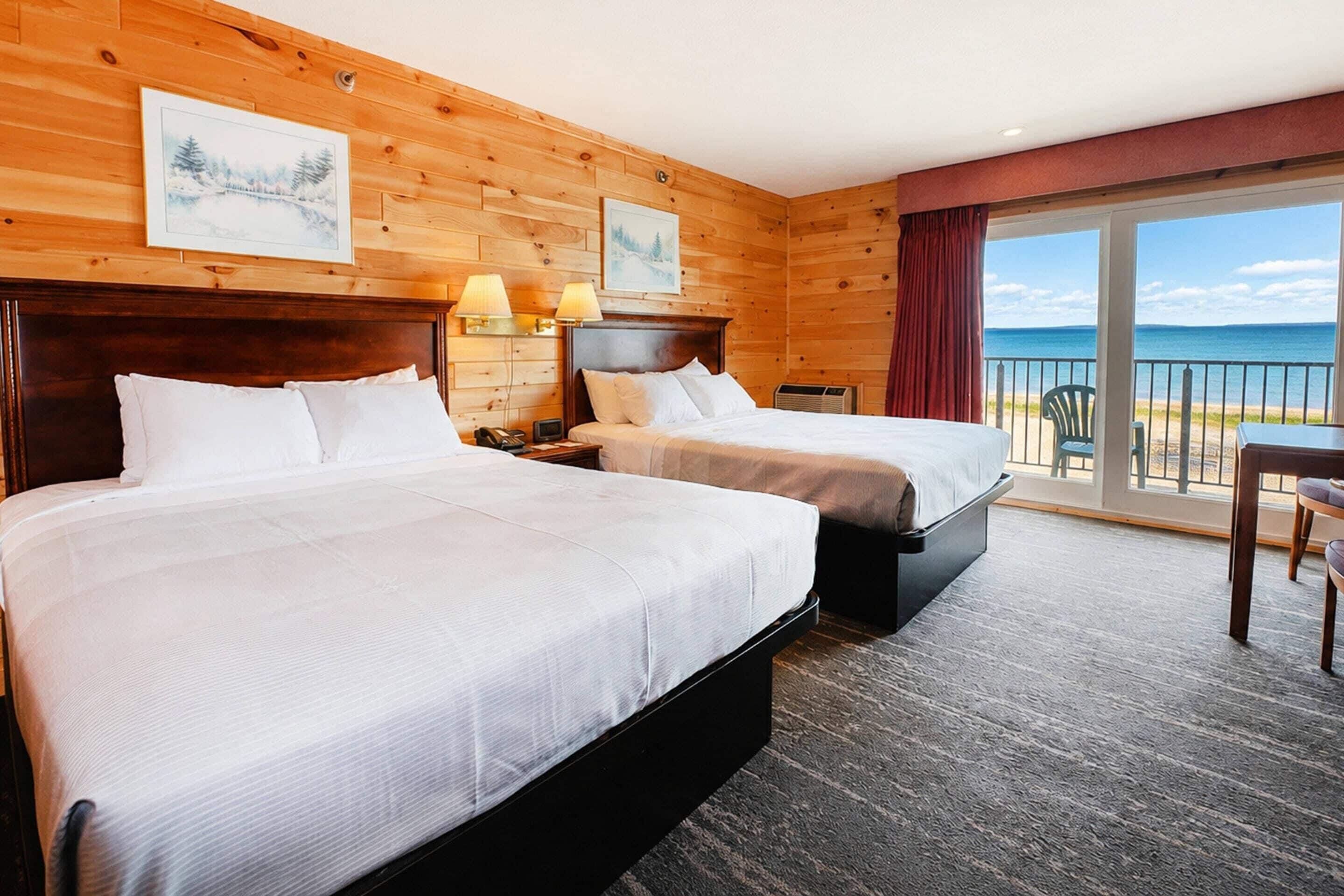 A hotel room with two beds, a desk, and a view of the sea.