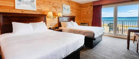 A hotel room with two beds, a desk, and a view of the sea.
