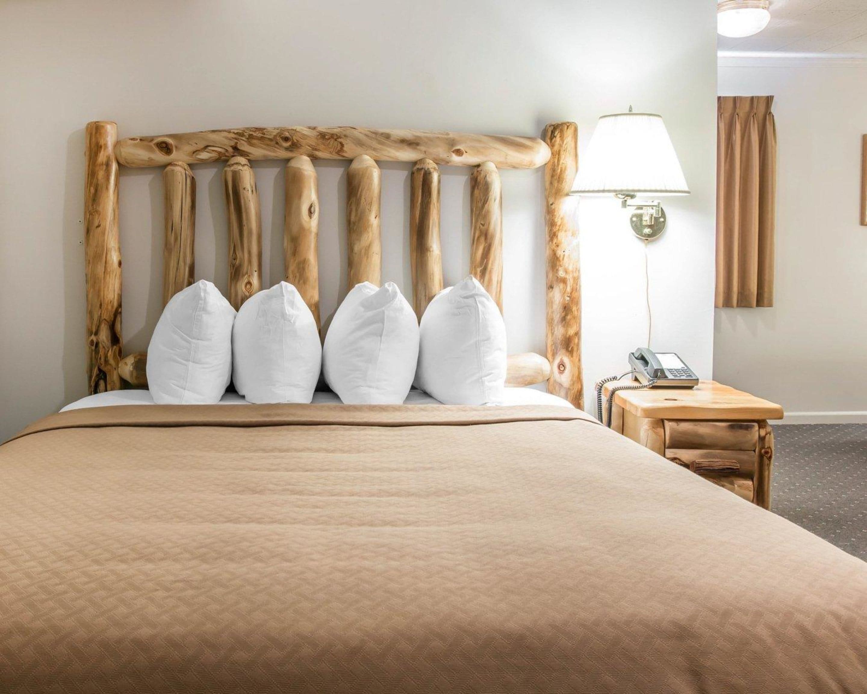 Hotelkamer met een houten hoofdbord, een bed met een beige sprei, witte kussens, een bedlampje en een telefoon op een nachtkastje van hout.