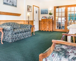 A room with a floral-patterned sofa, a wooden cabinet with brochures, and a view through a glass door. - Quality Inn & Suites Mackinaw City Beachfront (Mackinaw City)