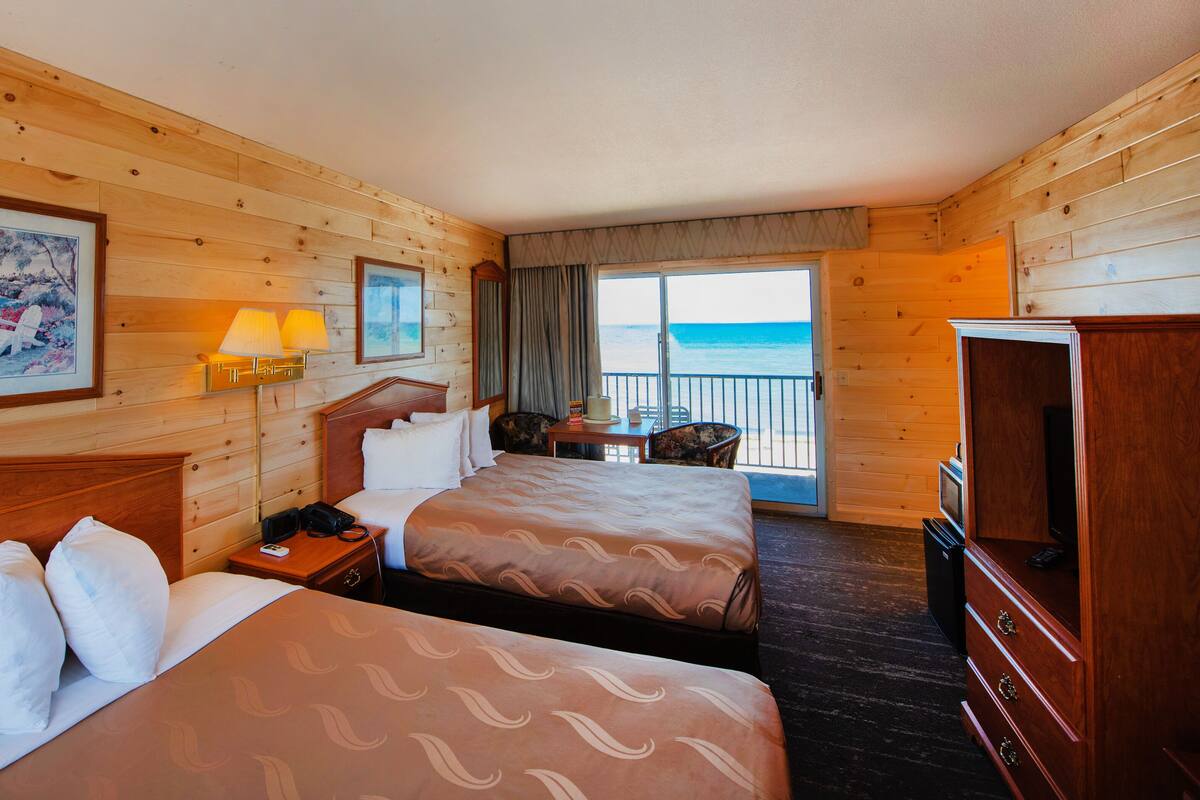 Habitación de hotel con dos camas, televisión, escritorio y balcón con vista al océano.