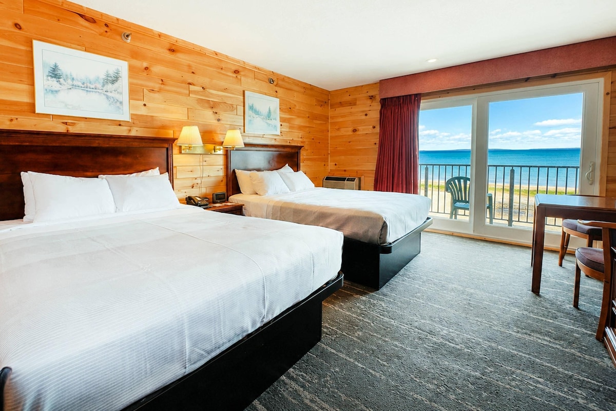 A hotel room with two beds, a desk, and a view of the sea.
