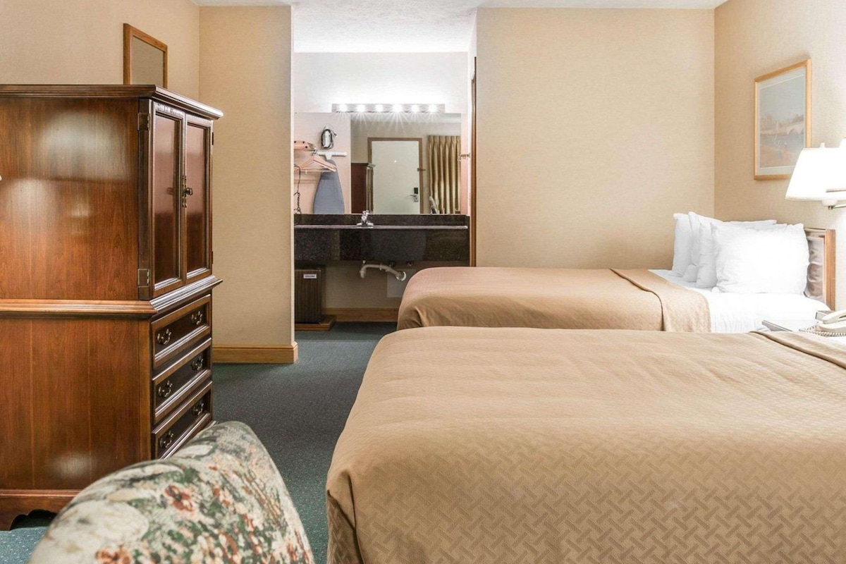 A hotel room with two beds, a dresser, a vanity with a mirror, and a bathroom visible through an open door.