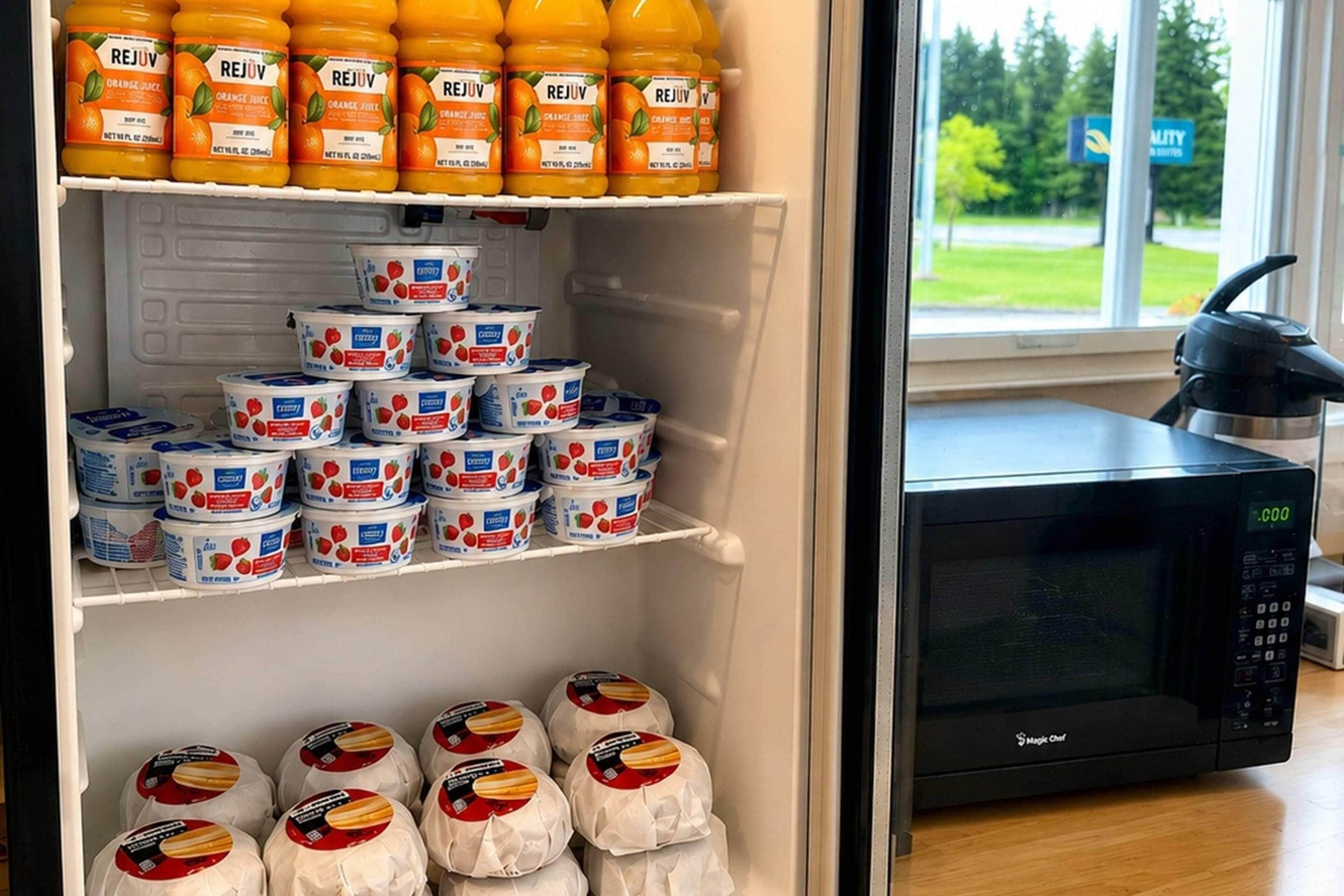 A refrigerator stocked with various food items, including orange juice and yogurt, with a microwave on the counter.