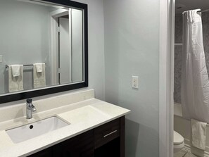A bathroom with a white sink, dark wooden cabinet, and a large mirror. - Motel 6 Greenville, NC – ECU-Medical Center (Greenville)