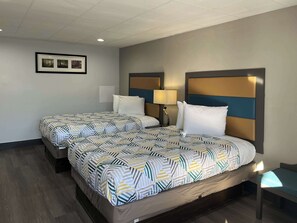 A hotel room with two beds, each with patterned bedding, a bedside table with a lamp, and a framed picture on the wall. - Motel 6 Greenville, NC – ECU-Medical Center (Greenville)
