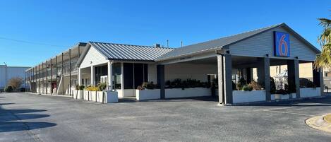 A motel with a covered parking area, a clear sky, and a sign indicating a maximum clearance of 9'7".
