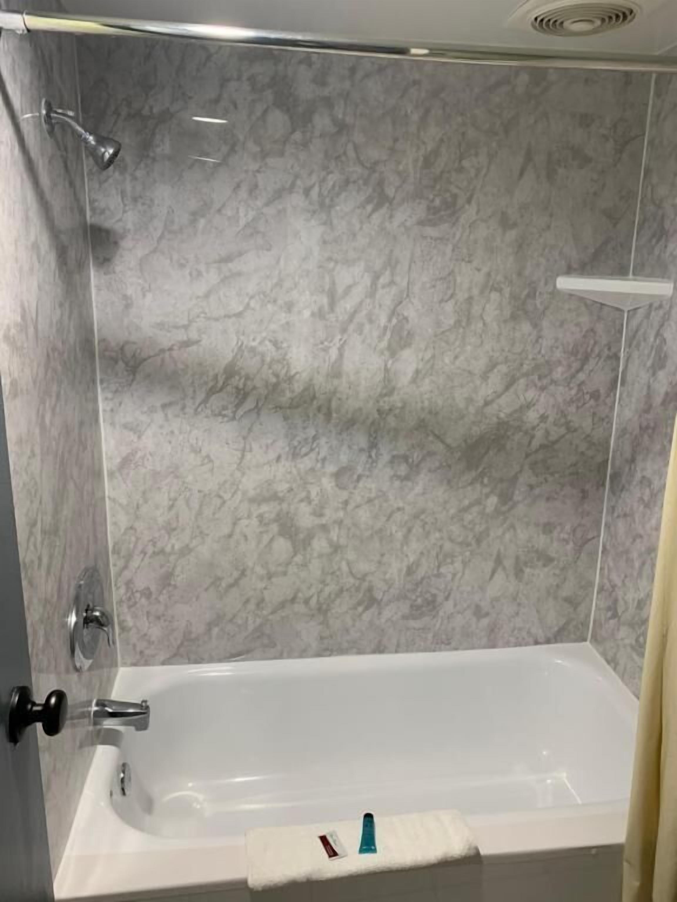 A bathroom with a white bathtub, marble walls, and a shower area.