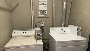 A laundry room with a front-loading washer and dryer, a sign detailing the cost and time for using the dryer, and a Whirlpool brand dryer. - Motel 6 Greenville, NC – ECU-Medical Center (Greenville)