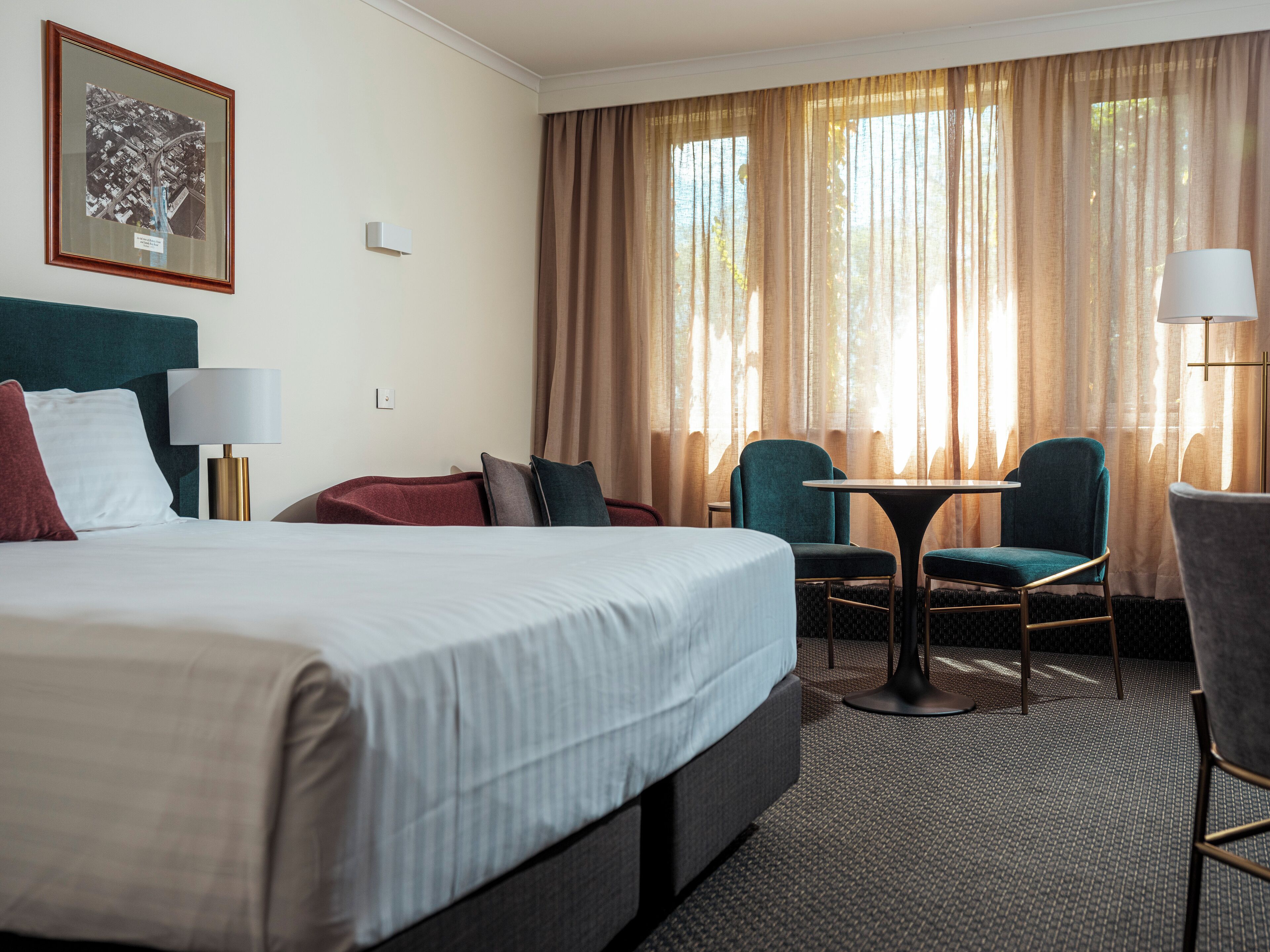 A hotel room with a large bed, two chairs, a small table, and a lamp.