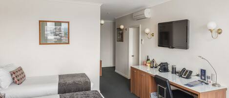 A hotel room with two beds, a desk with a computer, a TV, and a small kitchenette.
