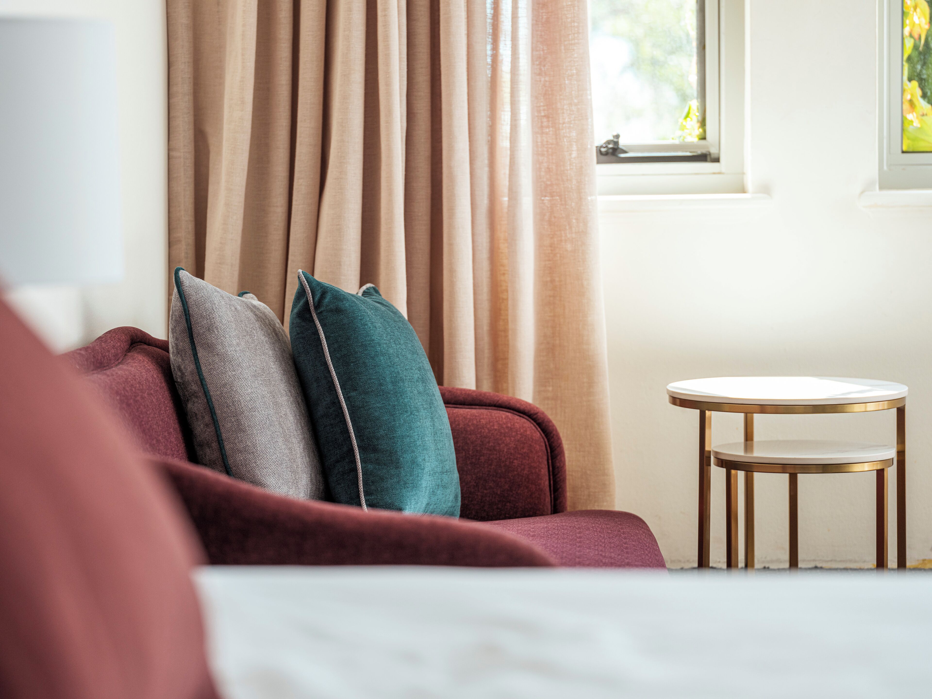 Habitación de hotel con un sofá rojo, una mesita redonda y cortinas color beige.