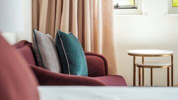 Habitación de hotel con un sofá rojo, una mesita redonda y cortinas color beige.