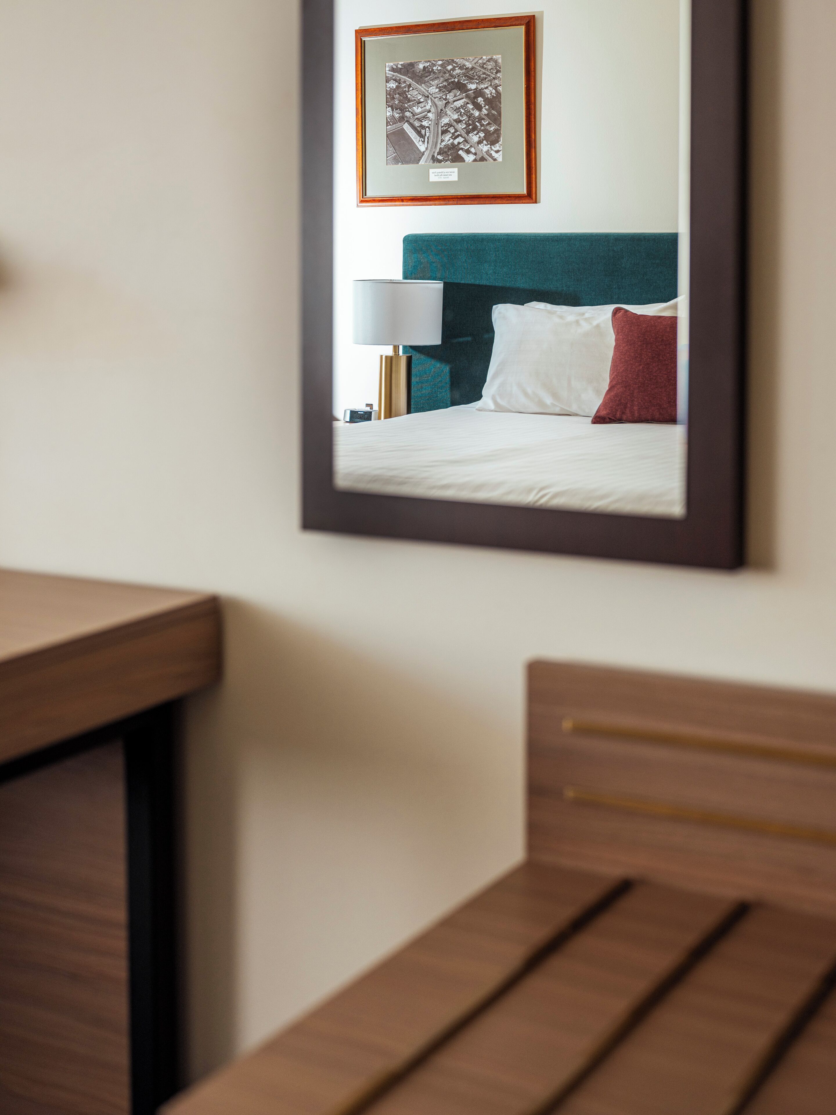 Una fotografía enmarco de una habitación de hotel con una cama, una mesita de noche y una lámpara.