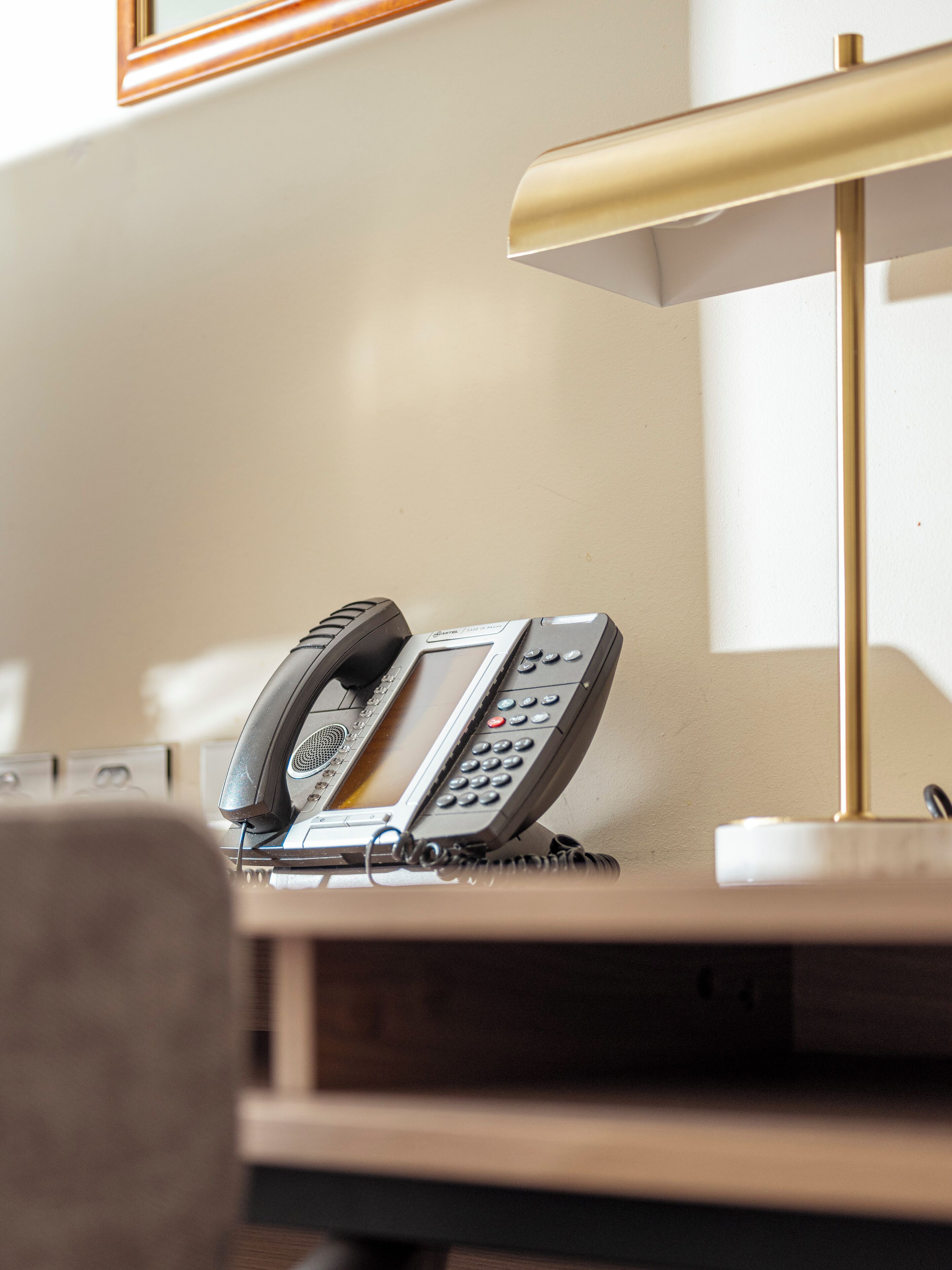 A desk with a telephone, a lamp, and a framed picture on the wall.