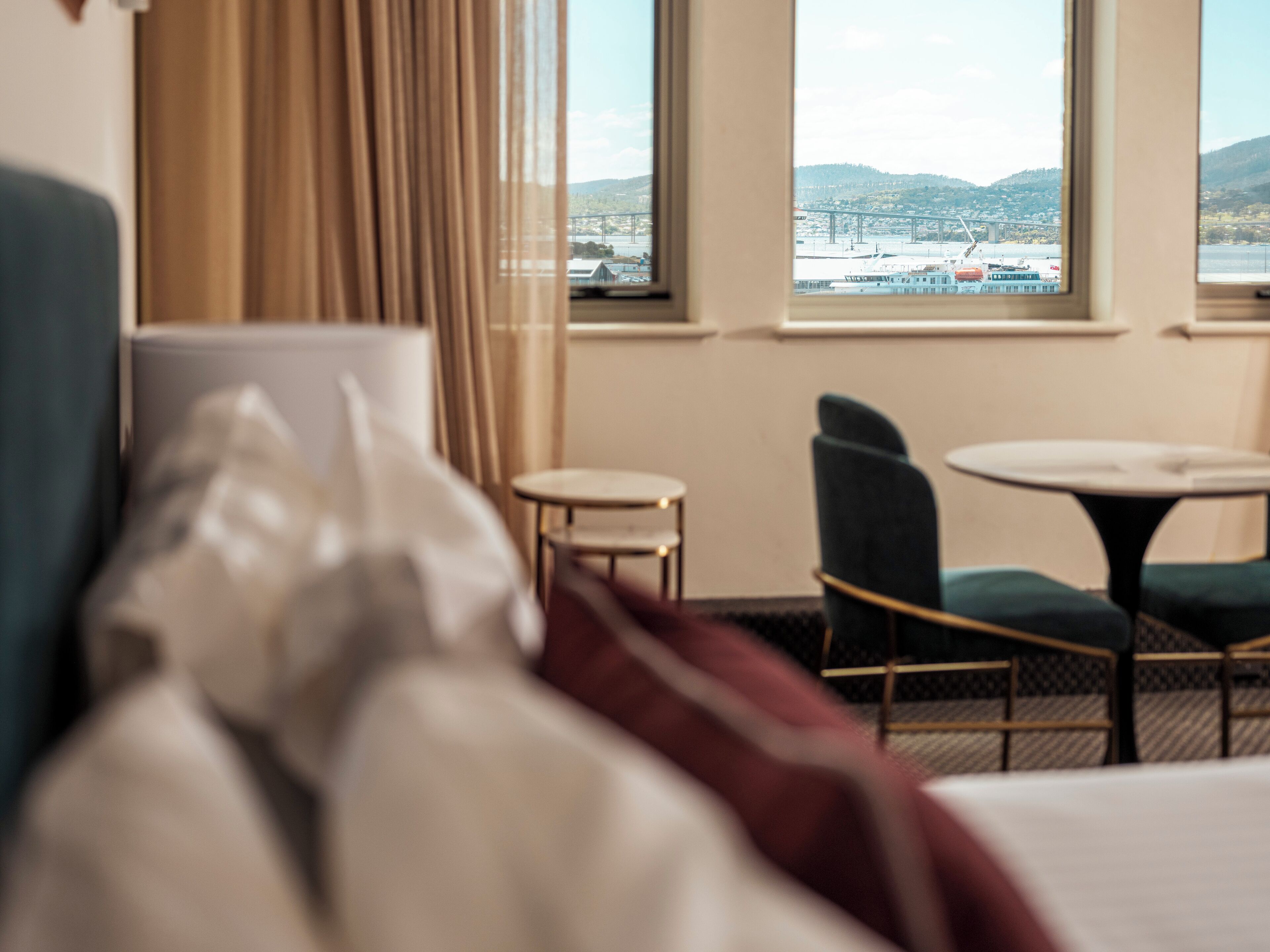 Une chambre d’hôtel avec un lit, une fenêtre donnant sur un pont et des collines, une petite table ronde et une chaise.