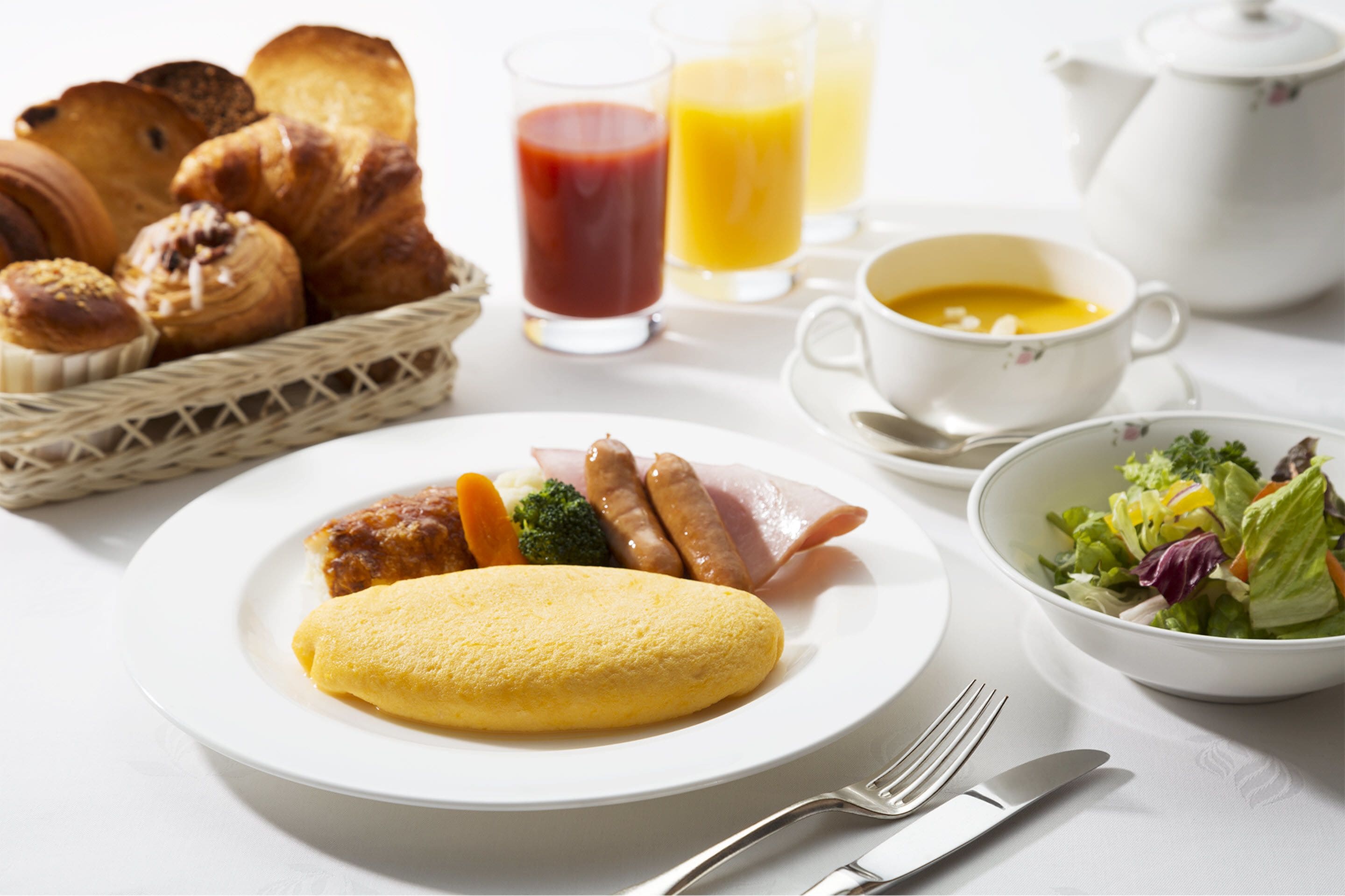 A breakfast setting with bread, eggs, sausages, vegetables, and a bowl of salad.
