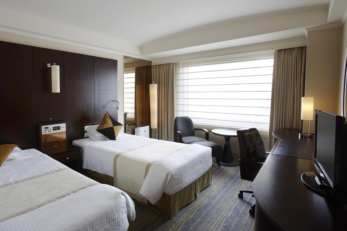 A hotel room with two beds, a desk, a chair, a TV, and a window with curtains.